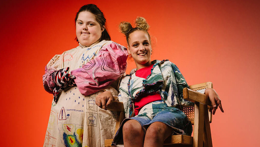 Two women together smiling against an orange background